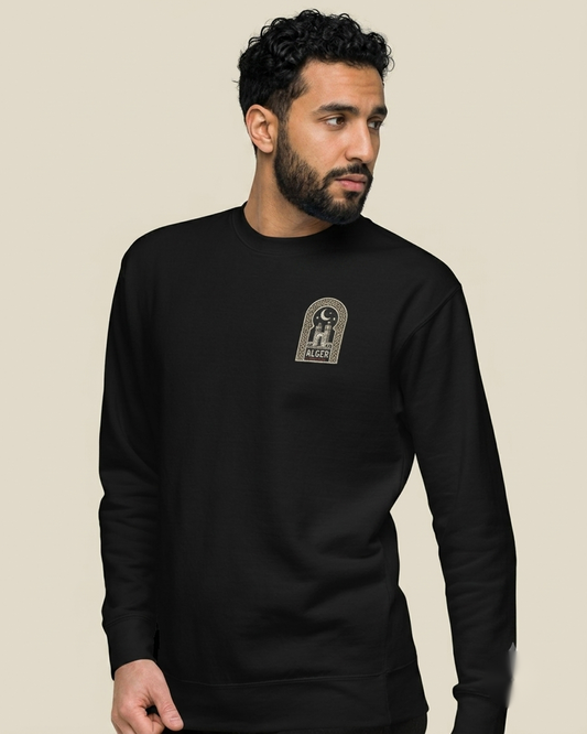 Homme nord-africain portant le sweatshirt Under the Stars noir qalbi, logo arche Alger avec croissant de lune et étoiles sur la poitrine